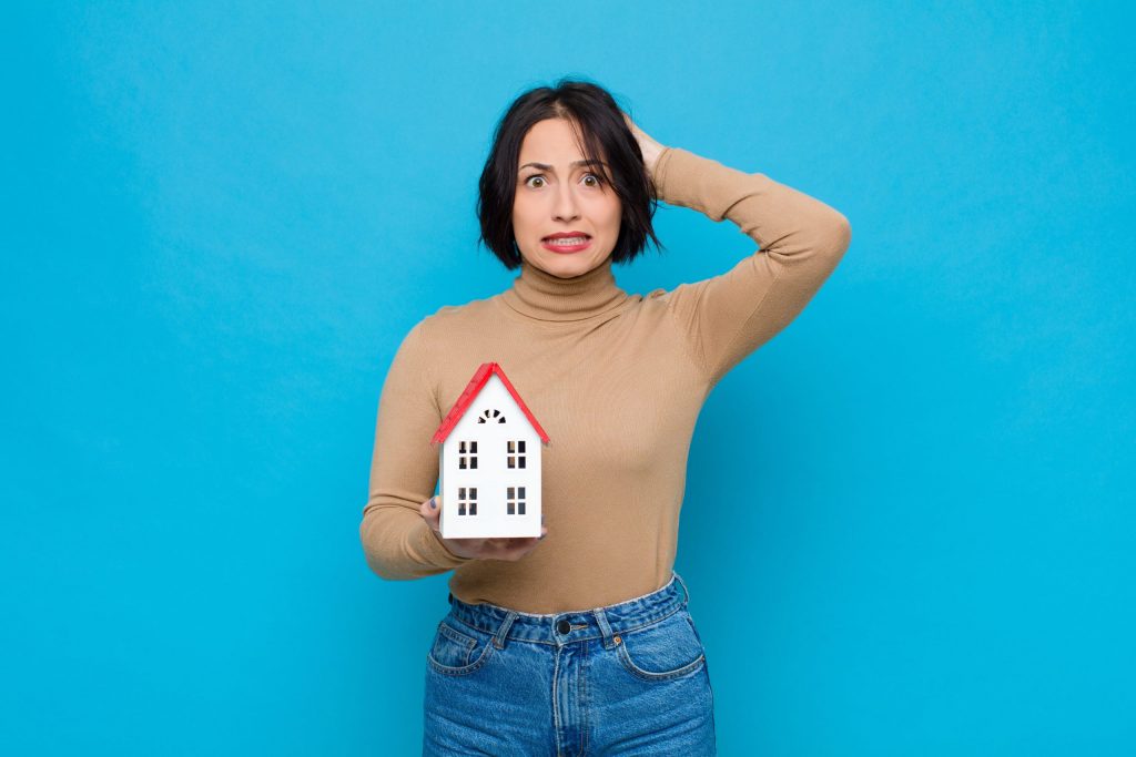 Mlada ženska z zaskrbljenim pogledom v rokah drži model hiše. 