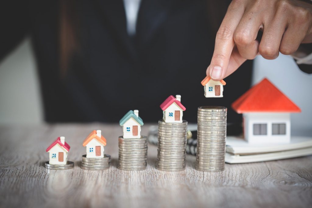 Roka postavlja model hiške na kup kovancev - koncept varčevanja denarja za nakup hipoteke na nepremičnino.