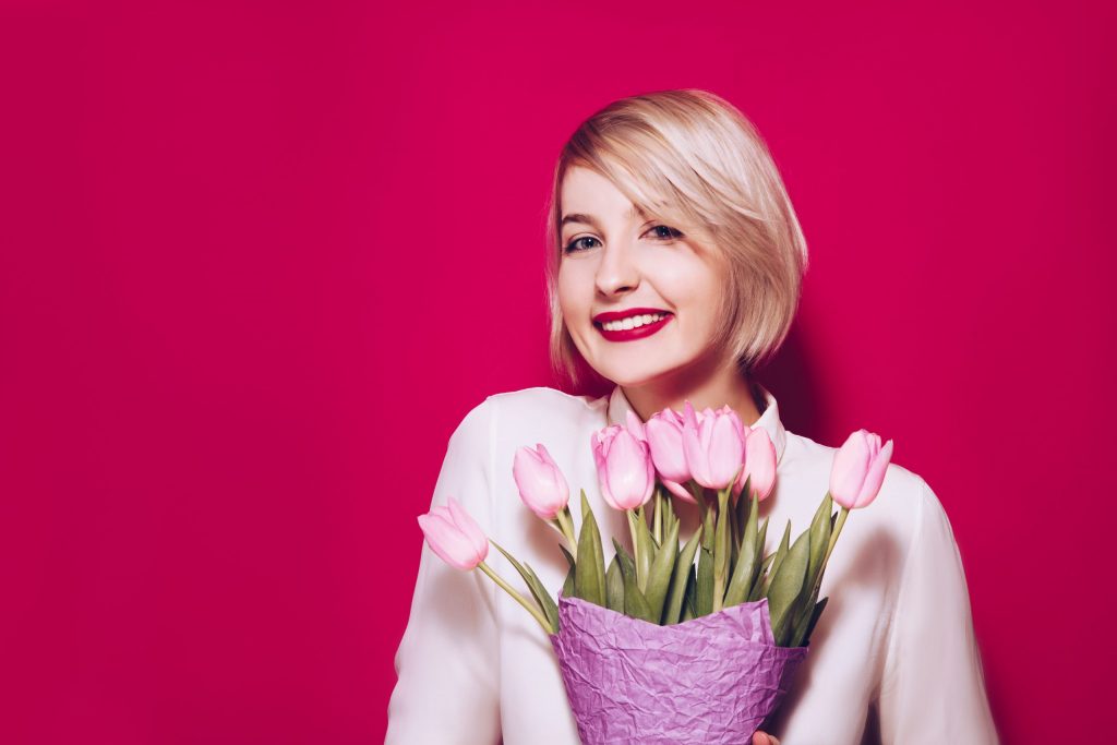 Nasmejana ženska drži šopek roza tulipanov.