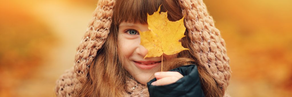 Nasmejana deklica si z javorjevim listom prekriva oko.