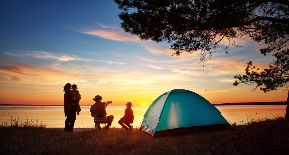 Družina uživa v sončnem zahodu ob jezeru, kjer so postavili šotor. 