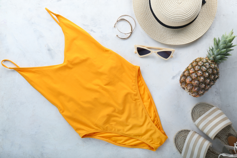 Poletni set: oranžne kopalke, ananas, natikači, slamnik in sončna očala. 